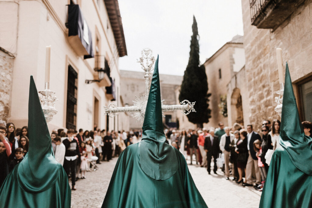 Foto del principio de una procesión, con los nazarenos vestidos de verde portando 2 ciriales y la cruz de guía